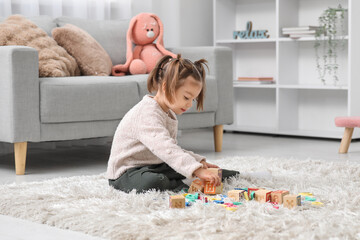 Cute little girl with cubes learning alphabet on carpet at home