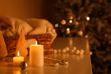 Burning candles and beautiful decorations on table against Christmas tree in room