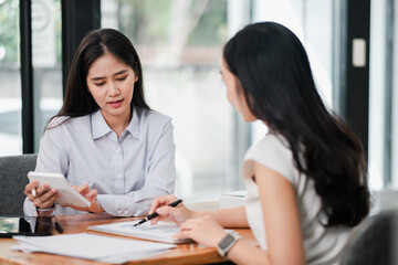 Two women engaged in a business meeting, reviewing documents and using a tablet in a contemporary office environment.