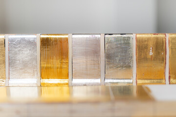Art conservator's gilding test tiles showcasing gold and silver leaf on various pulments, with different glazes and patinas. Perfect for illustrating restoration, art techniques, or material studies. © Anna Zaro