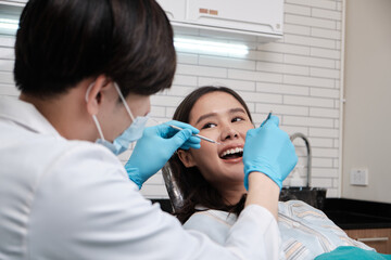 Fototapeta premium Asian male dentist examines beautiful young female patient's teeth stomatology in dental clinic, well-being hygiene checks, and professional orthodontic healthcare work in doctor's office hospital.