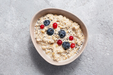 Bowl with tasty oatmeal, berries and chia seeds on grey grunge background