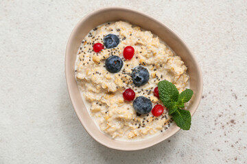 Bowl with tasty oatmeal, berries and chia seeds on beige grunge background