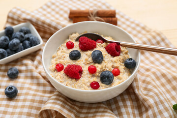 Bowl with tasty oatmeal and berries on napkin as background, closeup