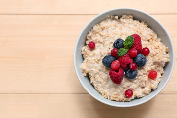 Bowl with tasty oatmeal and berries on wooden background