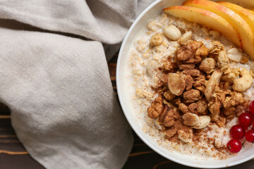 Bowl with tasty oatmeal, pieces of apple, berries and nuts on wooden background, closeup