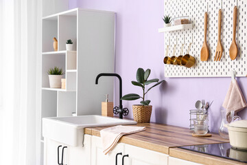 Interior of stylish kitchen with utensils on pegboard, sink and electric oven