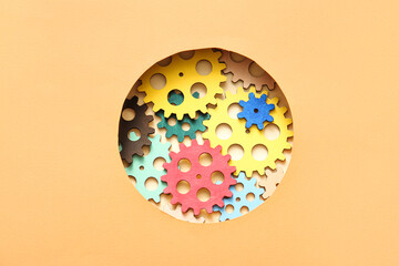 Wooden gears visible through round hole in orange paper