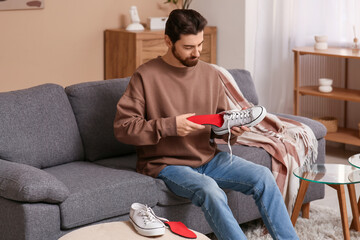 Young man putting red orthopedic insole into sneaker at home