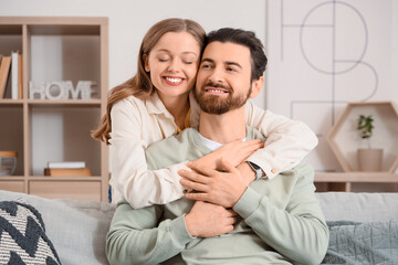 Apologizing young woman hugging her husband on sofa at home