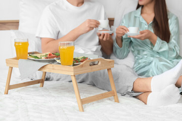 Young couple with cups of coffee having breakfast in bedroom