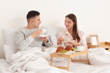 Young couple having breakfast in bed at home