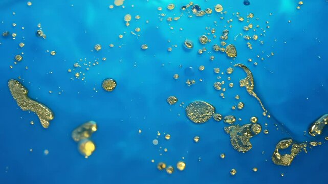 Dynamic drops of yellow glitter in blue oil or ink diffusing through water, creating an abstract aquatic swirls
