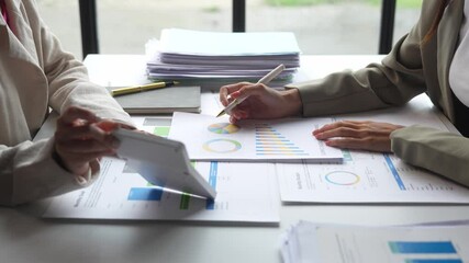 Two women are sitting at a table with papers and a pen. They are discussing something, possibly related to business or work. The atmosphere seems to be serious and focused