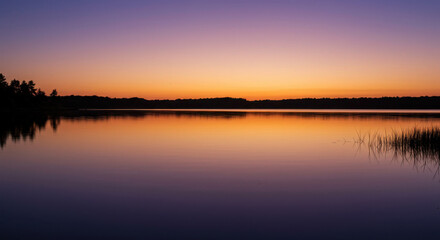 Naklejka premium A serene twilight sky reflected in a calm lake, with hues of deep purple and soft orange blending in the still waters