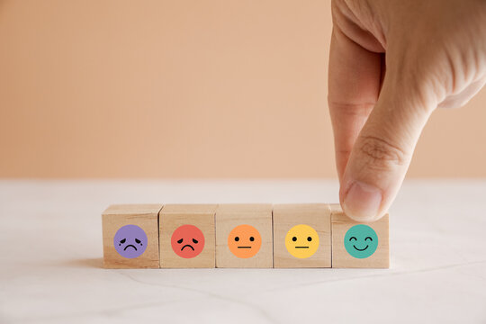 Hand choosing happy smile face wooden block, good feedback rating and positive customer review, mental health assessment, child wellness,world mental health day, think positive, compliment day concept