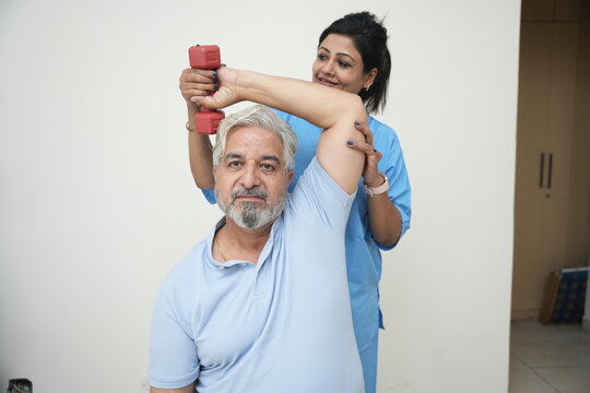 Indian physiotherapist help elderly man with dumbbell exercise to recover from injury at health center. Rehab fitness for senior patients concept, rehabilitation.