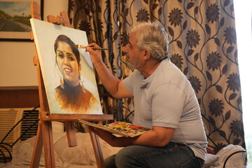 Indian creative senior artist man draw painting of woman on canvas with a brush and palette at home. Retirement life. Imagination, Creativity and art.