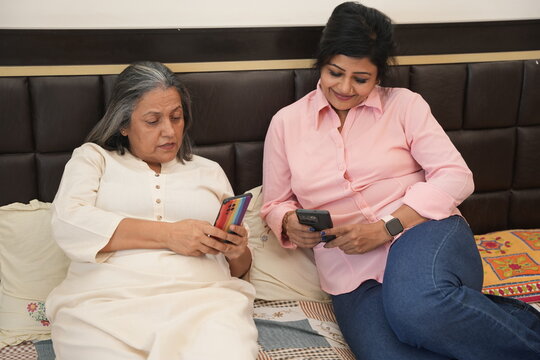 Indian mother and daughter using smart phone while lying in bed at home, watching and reading something, spending time together. Internet communication device, 5G Network, Technology. - Powered by Adobe