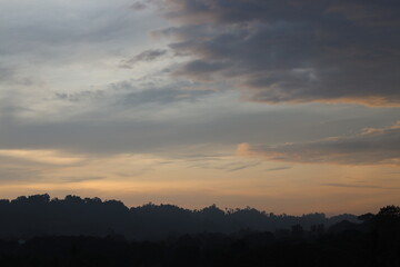 clouds painted in pastel hues of gold, pink, blue, gray (grey) above dense tropical rain forest at sunrise