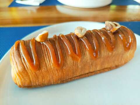 photo of an ecler cake on a white round plate decorated with nuts and caramel sauce and melted chocolate