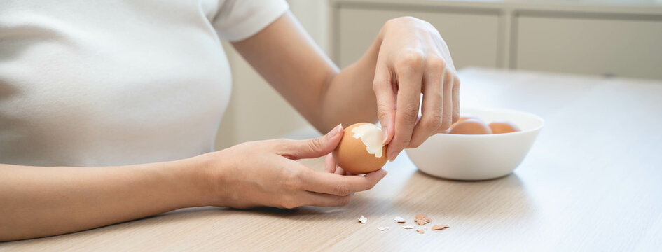 Close-up shot of woman hands peeling shell of boiled egg on the table.