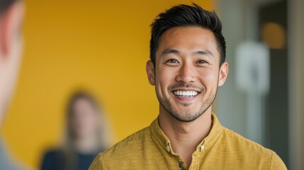Obraz premium A smiling man in a yellow shirt stands in front of a bright background, exuding confidence and positivity.
