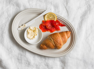Delicious breakfast, snack, brunch - croissant, lightly salted salmon, butter on a plate on a light background