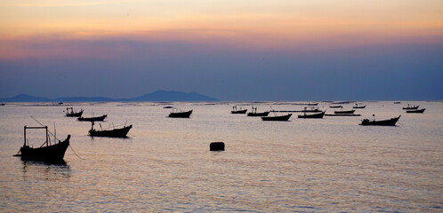 Naklejka premium Silhouette of fisherman boat mooring at bay with sunset sky and island background