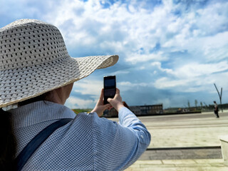 Person in a wide-brimmed hat capturing a photo of a scenic outdoor view on a sunny day