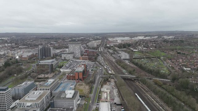 Aerial establishing view of Basingstoke's urban landscape, featuring high-rise buildings, busy roads, and mixed industrial-residential zones under soft light