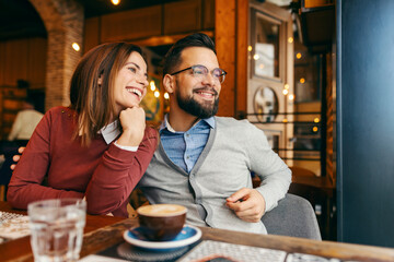 Happy romantic couple is hugging and looking trough the window in coffee shop.