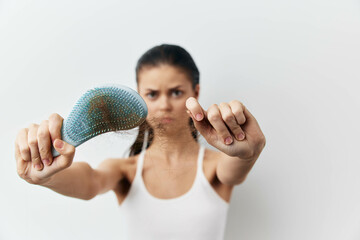 Woman showing hair loss with a hairbrush against a white background, expressing frustration and...