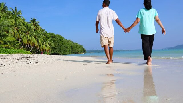 married couple romantic walk with holding hands strolling along beach with rolling waves at morning video is taken at Radhanagar Beach at Havelock Island in the Andaman and Nicobar Islands.