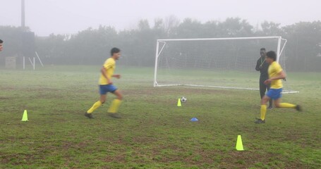 Soccer players training on field with cones and coach in foggy weather - Powered by Adobe