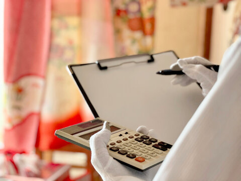 クリップボードと計算機を持って着物を査定する人