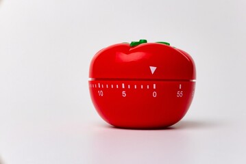 Close up view of mechanical tomato shaped kitchen clock timer for cooking and studying. Used for pomodoro technique for time & productivity management. Isolated on white background, set at 5 minutes.