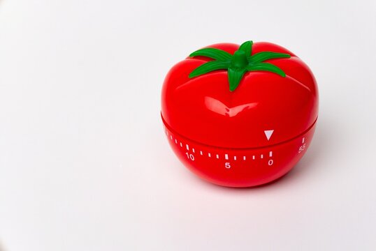Close up view of mechanical tomato shaped kitchen clock timer for cooking and studying. Used for pomodoro technique for time & productivity management. Isolated on white background, set at 5 minutes.
