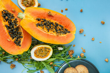 Papaya, passion fruit, rucola and granola on a blue background. Slices of sweet papaya, passion fruit, granola and rucola on blue background, Halved papayas, copy space for text, healthy food