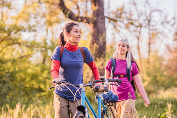 Fototapeta premium Two female friends walking with bicycles in nature during golden hour