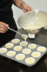 Pouring cupcake batter to cupcake paper on a baking pan