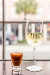 Glass of white wine and an oyster shooter by a during happy hour.