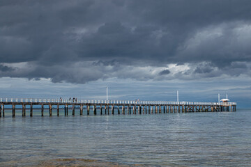 Long pier over calm water under stormy skies Point Lonsdale Pier
