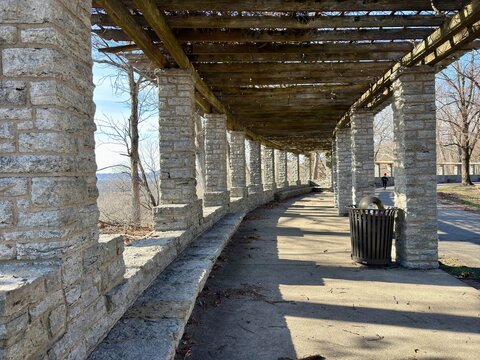Stone pergola with wooden beams and shadows on a paved path in a park