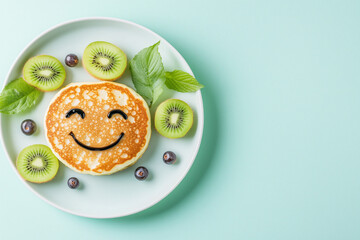 A plate of food with a smiling face made out of pancakes and kiwi slices