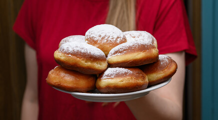 Dziewczyna trzymająca talerz pełny słodkich pączków drożdżowych posypanych cukrem pudrem 