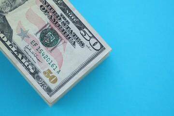Big amount of fifty dollar bills in thick stack lies on bright blue color paper background