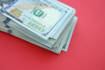 Big amount of hundred dollar bills in thick stack lies on bright red color paper background
