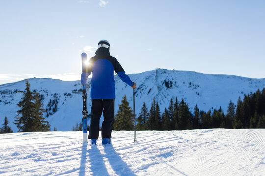 Skier overlooking Kitzb&uuml;hel Alps, holding skis on a sunny winter day