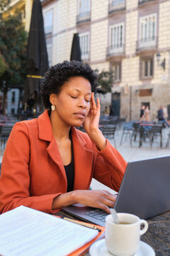 Stressed woman having headache while working on laptop at outdoor cafe